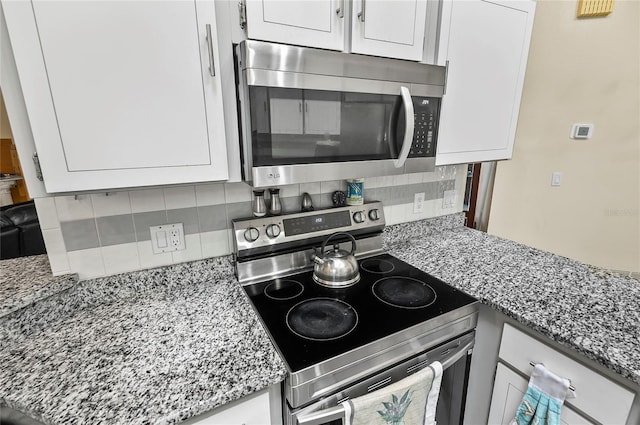 kitchen with decorative backsplash, stainless steel appliances, white cabinetry, and light stone countertops