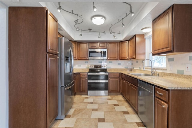 kitchen with light stone counters, track lighting, sink, backsplash, and appliances with stainless steel finishes