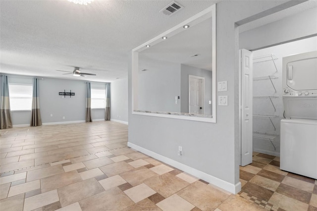 spare room featuring stacked washing maching and dryer, ceiling fan, and a textured ceiling