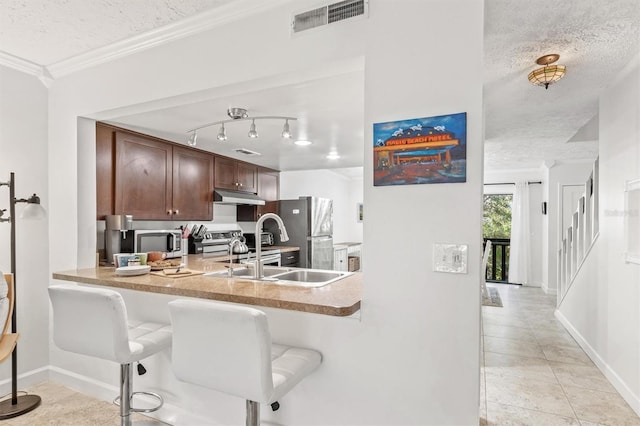 kitchen featuring a kitchen bar, a textured ceiling, stainless steel appliances, crown molding, and sink