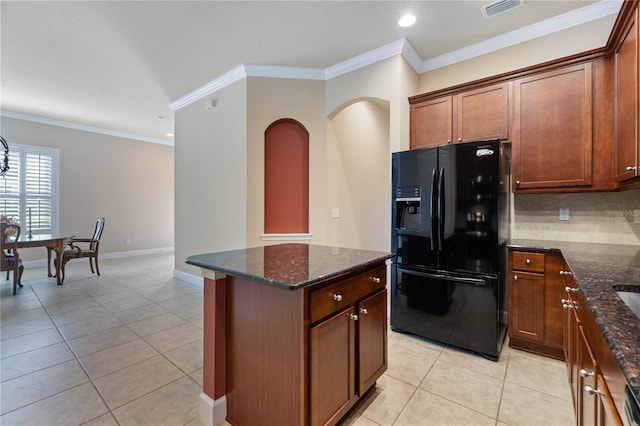 kitchen featuring light tile patterned floors, dark stone counters, black fridge, and crown molding