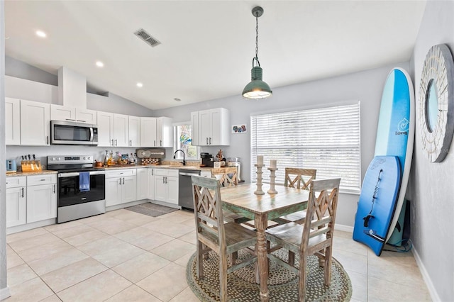 kitchen with stainless steel appliances, vaulted ceiling, hanging light fixtures, light tile patterned floors, and white cabinetry