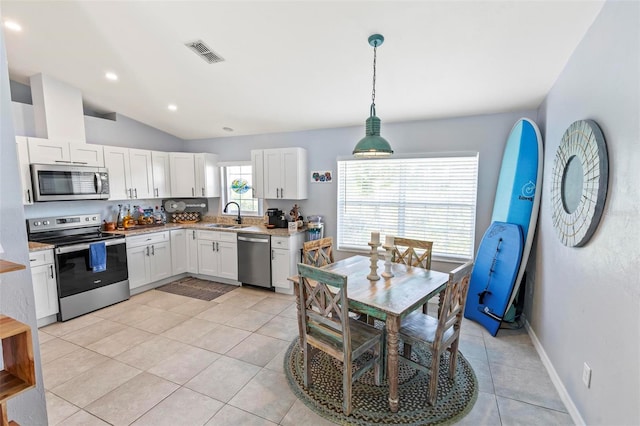 kitchen featuring stainless steel appliances, lofted ceiling, white cabinets, sink, and decorative light fixtures