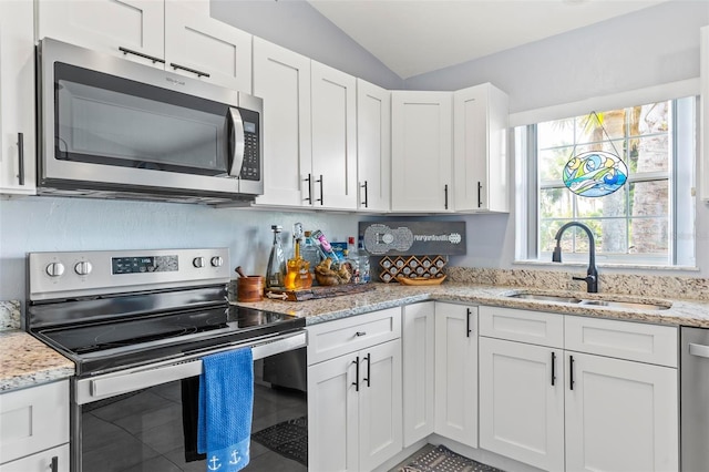 kitchen with lofted ceiling, light stone counters, white cabinets, sink, and appliances with stainless steel finishes