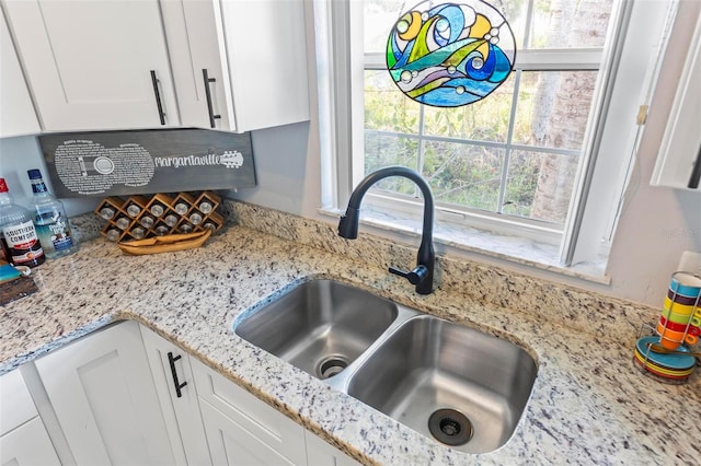 interior details with white cabinetry, sink, and light stone counters