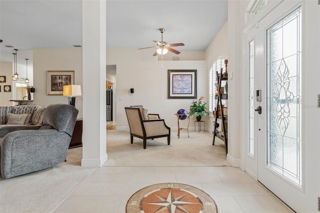 foyer entrance with ceiling fan, light carpet, and decorative columns