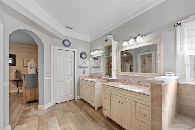 full bathroom featuring crown molding, two vanities, a sink, and wood finished floors