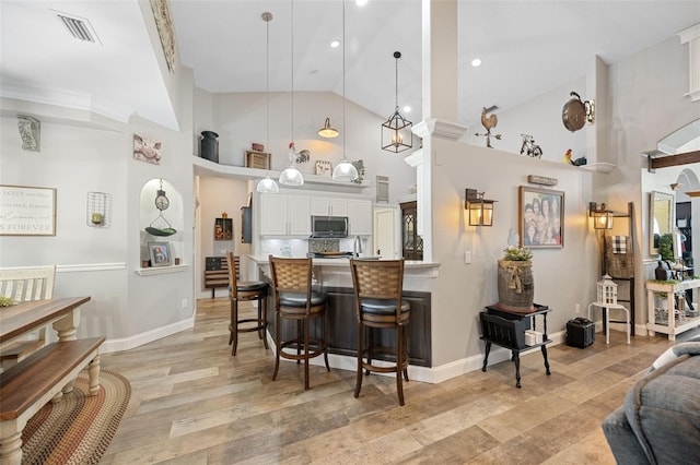 kitchen with light wood finished floors, visible vents, white cabinets, stainless steel microwave, and a breakfast bar area