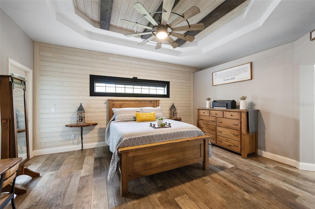 bedroom featuring baseboards, hardwood / wood-style flooring, ceiling fan, a tray ceiling, and wood walls