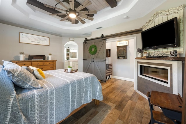 bedroom featuring a barn door, visible vents, baseboards, wood-type flooring, and a tray ceiling