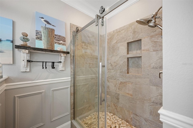 full bathroom featuring a stall shower, a decorative wall, crown molding, and a wainscoted wall