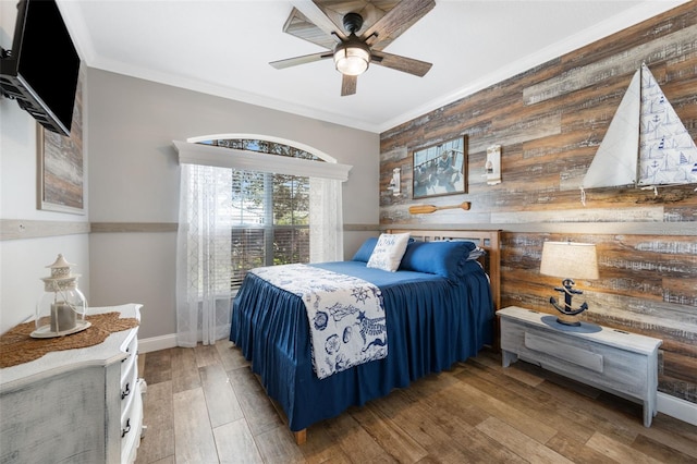 bedroom featuring crown molding, wooden walls, baseboards, and wood finished floors