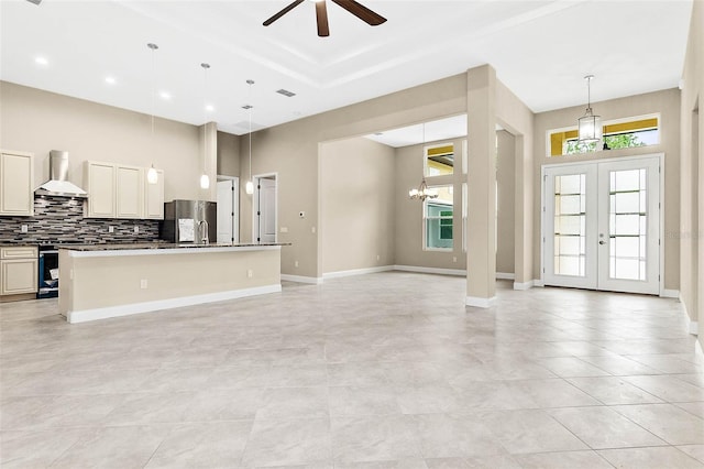 kitchen featuring french doors, wall chimney exhaust hood, an island with sink, pendant lighting, and stainless steel fridge