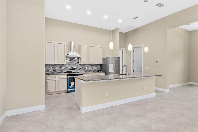 kitchen with stone countertops, sink, appliances with stainless steel finishes, an island with sink, and wall chimney range hood