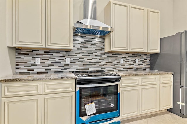 kitchen featuring stainless steel appliances, cream cabinets, tasteful backsplash, and wall chimney range hood