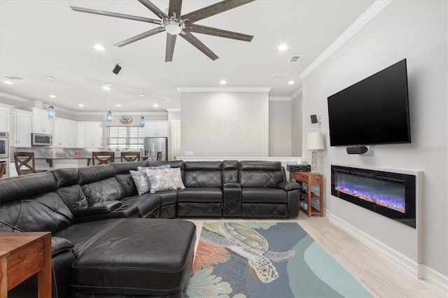 living area featuring recessed lighting, visible vents, light wood-style flooring, ornamental molding, and a glass covered fireplace