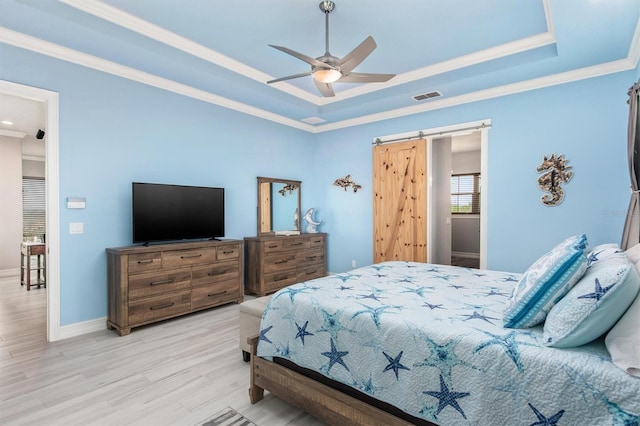 bedroom with a tray ceiling, a barn door, visible vents, and crown molding