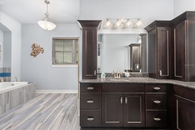 full bath featuring baseboards, vanity, a bath, and wood finished floors