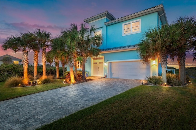 mediterranean / spanish-style home featuring an attached garage, stucco siding, decorative driveway, and a front yard