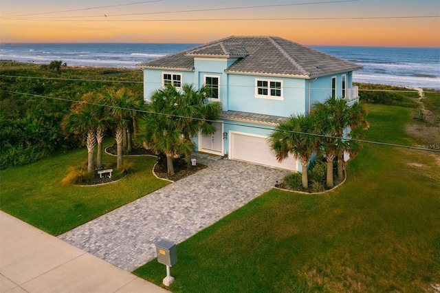 view of front of home with decorative driveway, stucco siding, a lawn, an attached garage, and a tiled roof