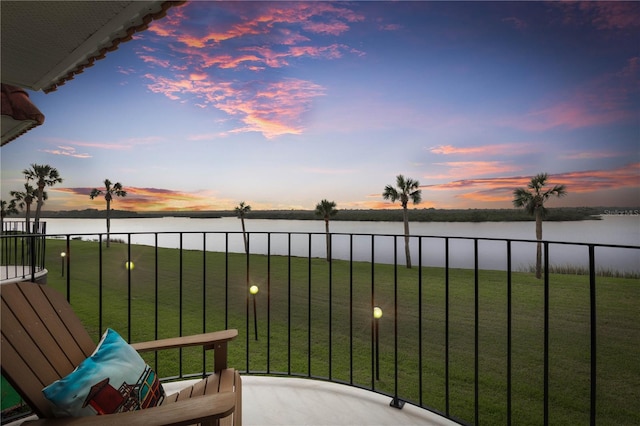 balcony at dusk featuring a water view