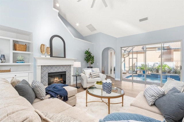 living room featuring a fireplace, ceiling fan, light wood-type flooring, and high vaulted ceiling