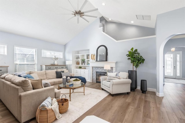 living room with light wood-type flooring, a fireplace, ceiling fan, and high vaulted ceiling