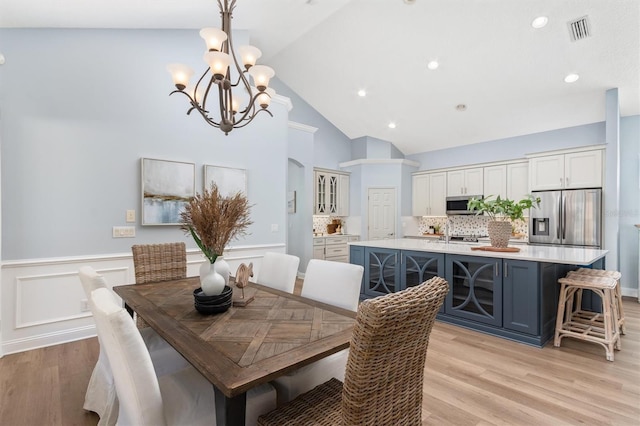 dining area featuring light hardwood / wood-style floors, high vaulted ceiling, and a notable chandelier