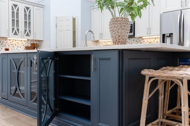 kitchen with white cabinetry, backsplash, stainless steel refrigerator with ice dispenser, and light wood-type flooring