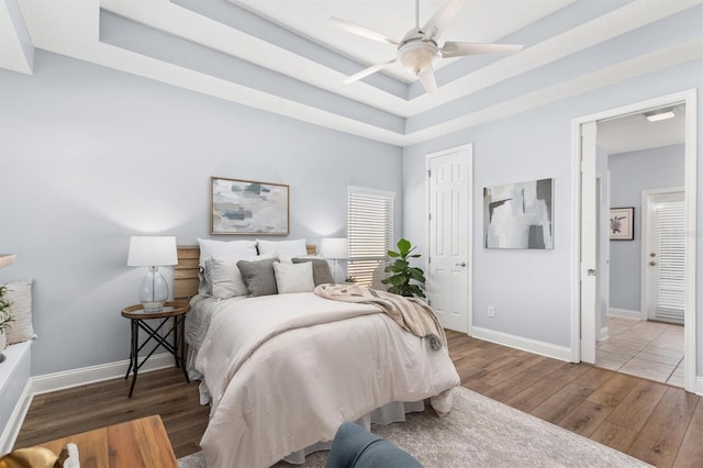 bedroom with dark hardwood / wood-style flooring, a tray ceiling, and ceiling fan