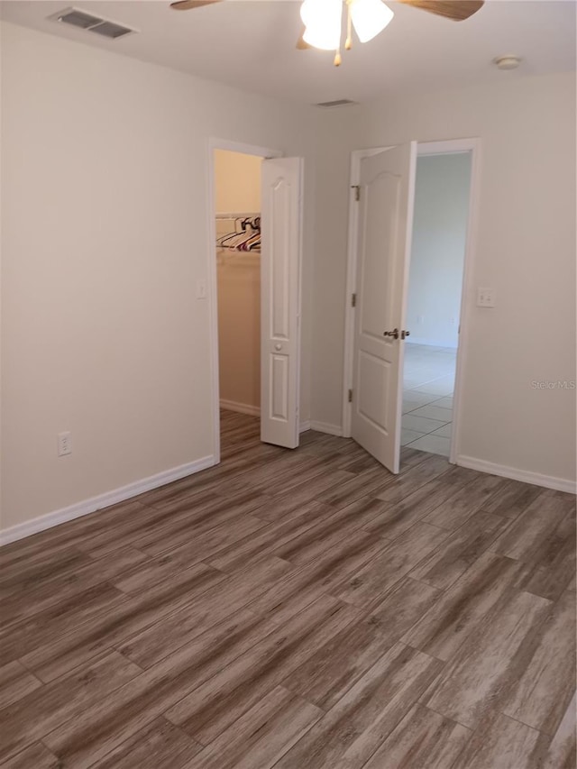 unfurnished bedroom with ceiling fan, a walk in closet, a closet, and dark hardwood / wood-style floors