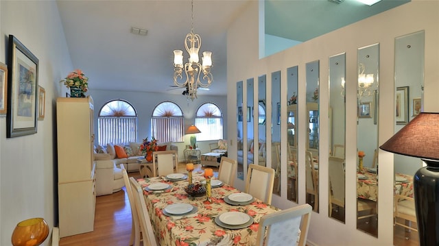 dining space with light hardwood / wood-style flooring, vaulted ceiling, and an inviting chandelier