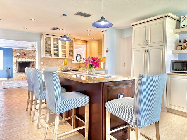 kitchen featuring hanging light fixtures, light stone counters, cream cabinetry, a breakfast bar area, and light wood-type flooring