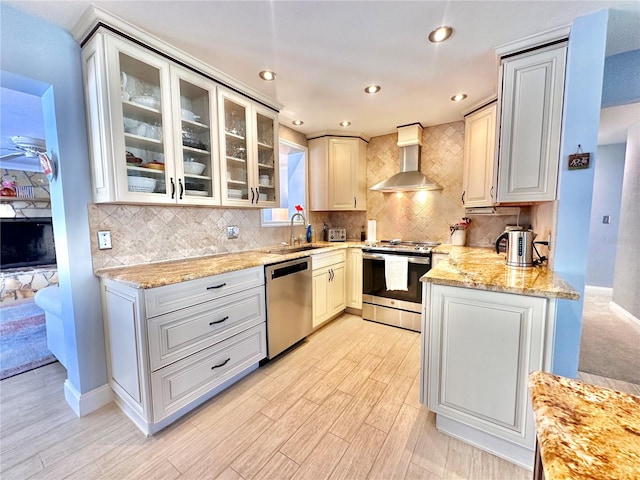 kitchen featuring sink, wall chimney range hood, tasteful backsplash, appliances with stainless steel finishes, and light wood-type flooring