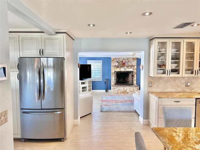 kitchen with a stone fireplace, light hardwood / wood-style flooring, tasteful backsplash, light stone counters, and stainless steel refrigerator