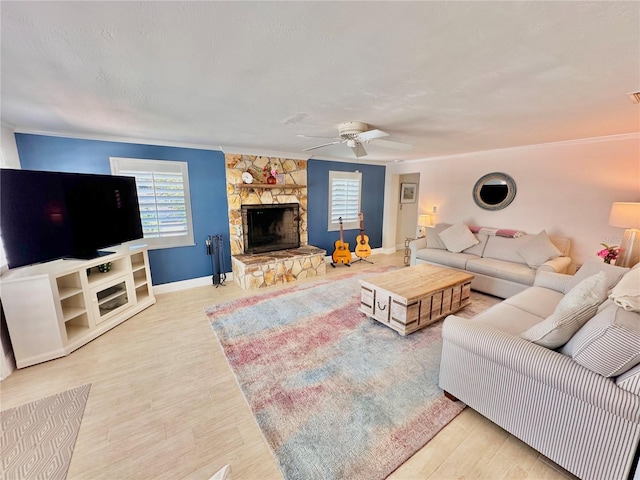 living room with a stone fireplace, ceiling fan, light hardwood / wood-style floors, and ornamental molding