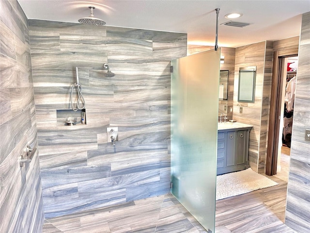 bathroom featuring a shower, vanity, and tile walls