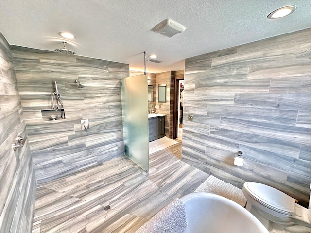 bathroom featuring vanity, a textured ceiling, a shower, tile walls, and toilet