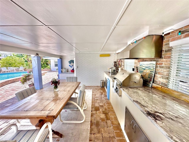 kitchen featuring a paneled ceiling, light stone countertops, white cabinets, and brick wall