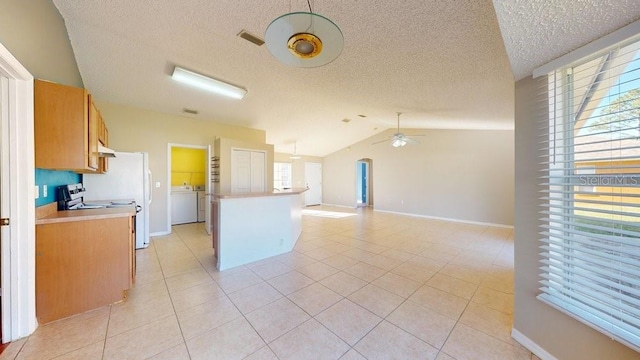 kitchen with ceiling fan, washer / clothes dryer, stove, vaulted ceiling, and light tile patterned floors