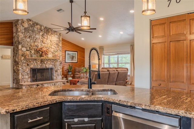 kitchen featuring sink, lofted ceiling, wooden walls, pendant lighting, and dishwasher