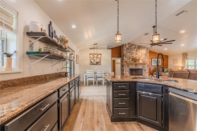 kitchen with a stone fireplace, light wood-type flooring, pendant lighting, dishwasher, and lofted ceiling