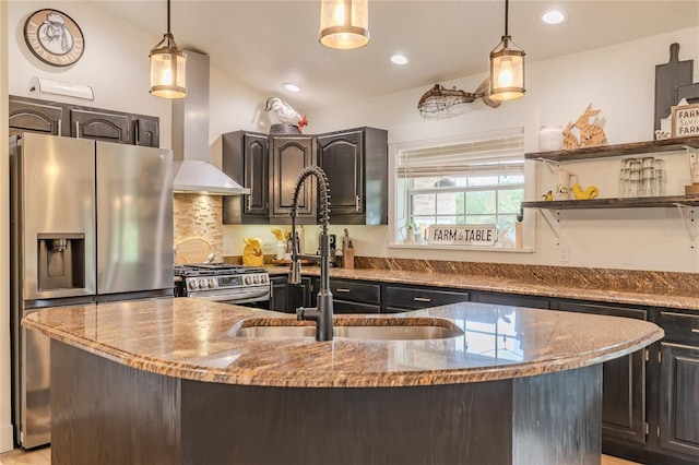 kitchen with stainless steel appliances, hanging light fixtures, sink, a kitchen island with sink, and light stone countertops