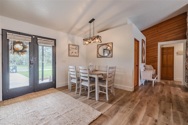 dining area with hardwood / wood-style floors, wooden walls, vaulted ceiling, and french doors