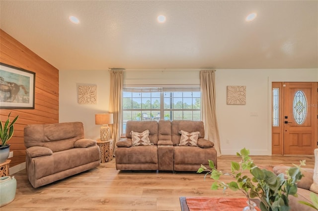 living room with light hardwood / wood-style floors, wood walls, and lofted ceiling