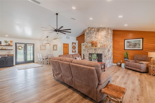 living room with a stone fireplace, vaulted ceiling, wood walls, ceiling fan, and light wood-type flooring