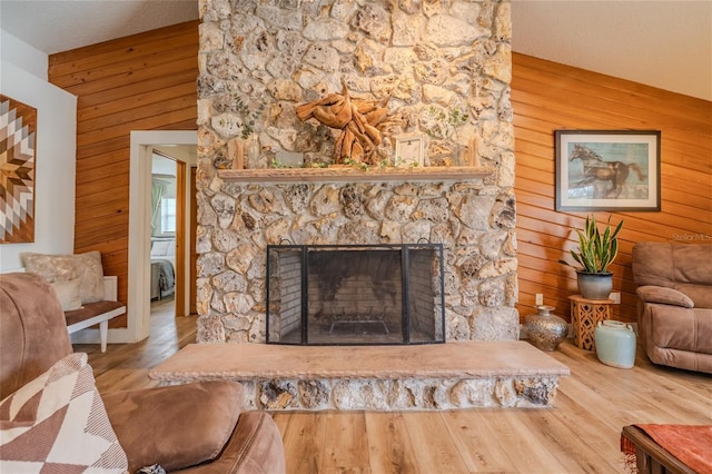 living room with wood walls, a stone fireplace, a textured ceiling, and hardwood / wood-style floors