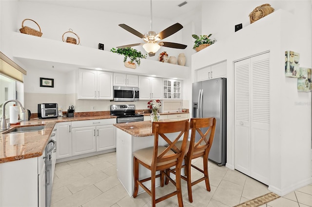 kitchen with stainless steel appliances, white cabinetry, high vaulted ceiling, light stone countertops, and sink