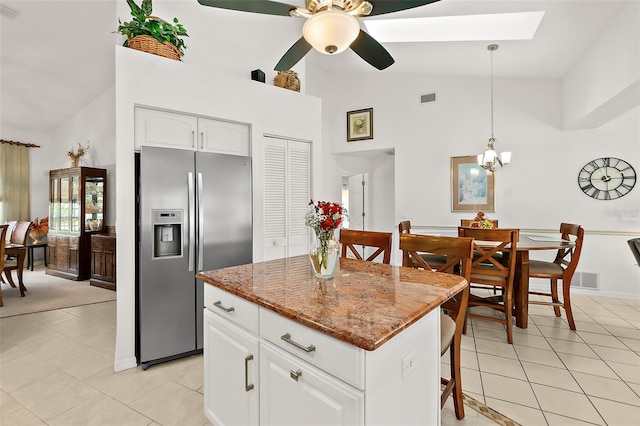 kitchen with light stone counters, a kitchen island, decorative light fixtures, stainless steel fridge with ice dispenser, and white cabinets