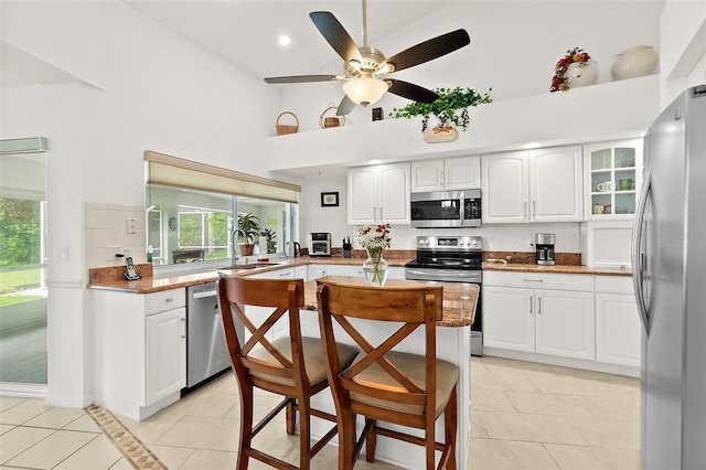 kitchen with white cabinets, high vaulted ceiling, light tile patterned floors, and appliances with stainless steel finishes